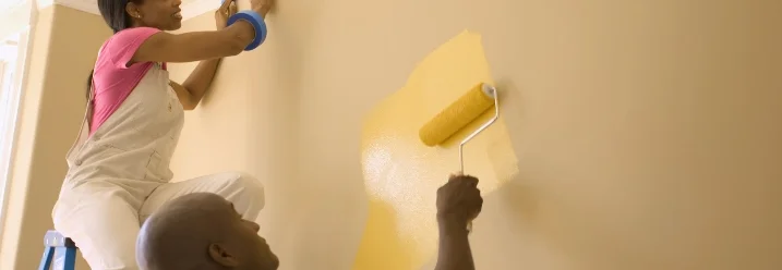 Zwei Personen streichen eine Wand gelb.